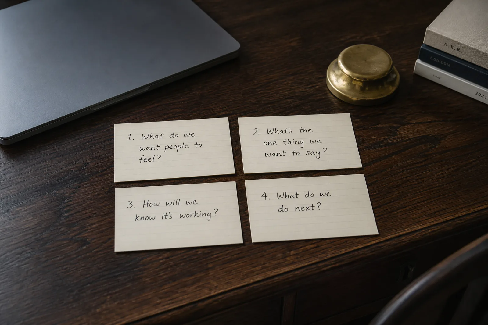 Four handwritten questions on cream index cards on an oak desk